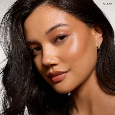 {Surge} Model wearing Morphe Complexion Boost Peptide Bronzing Serum in Surge, showing a dewy, bronzed complexion